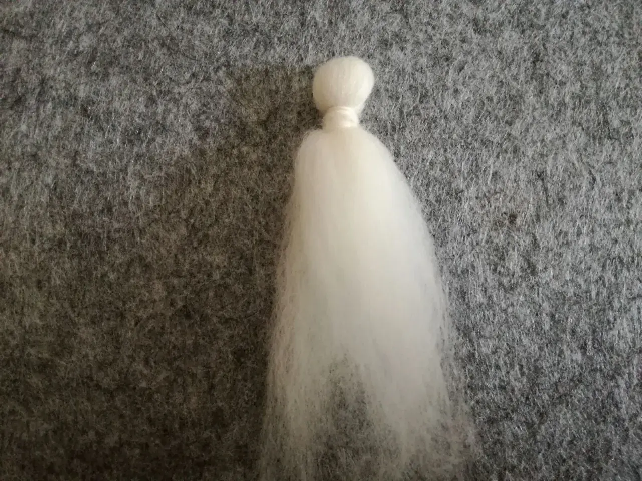 Ein weißer Wattebausch, der wie ein Kopf und ein Kleid aussieht, liegt auf grauem Filz. Dies ist der Anfang vom engel filzen.