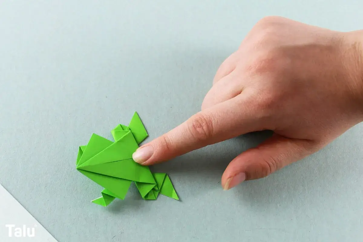 Grüner Origami-Frosch, der von einer Hand gehalten wird. Ein tolles Bastelprojekt für origami kinder.