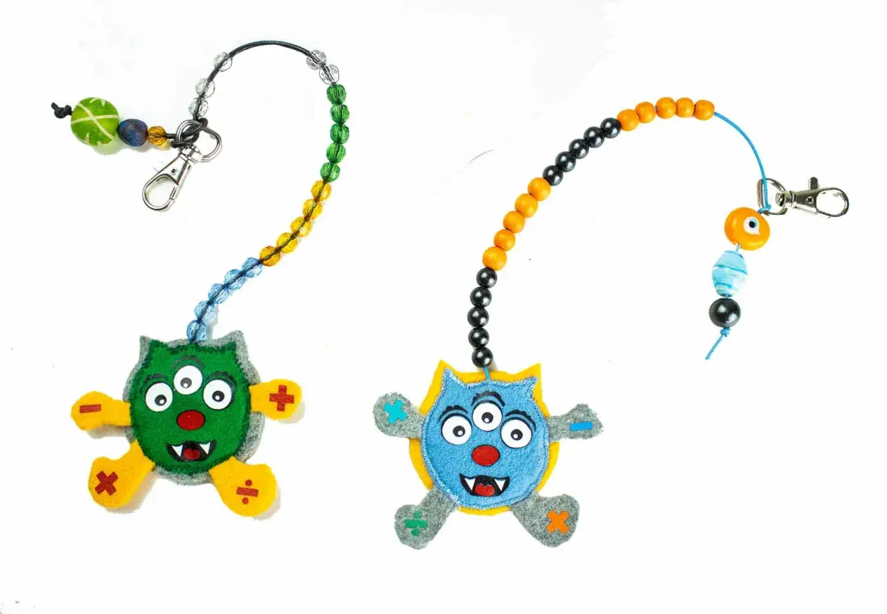 Zwei lustige Monster-Anhänger mit Perlenketten zum **rechenkette basteln**. Ein grünes und ein blaues Monster mit mathematischen Symbolen an den Füßen.