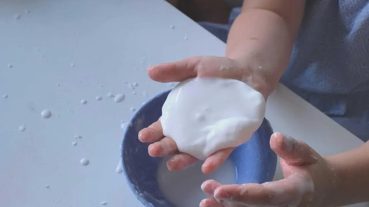 Kinderhände spielen mit weißer, klebriger Masse, die wie Oobleck-Rezept aussieht.