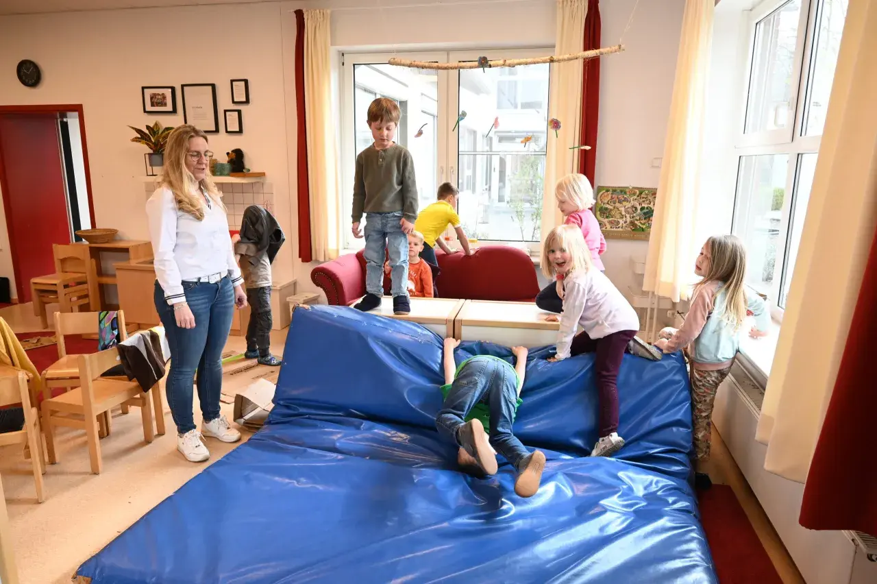 Kinder genießen spielzeugfreie Zeit in der Kita, klettern und toben auf einer blauen Matte.