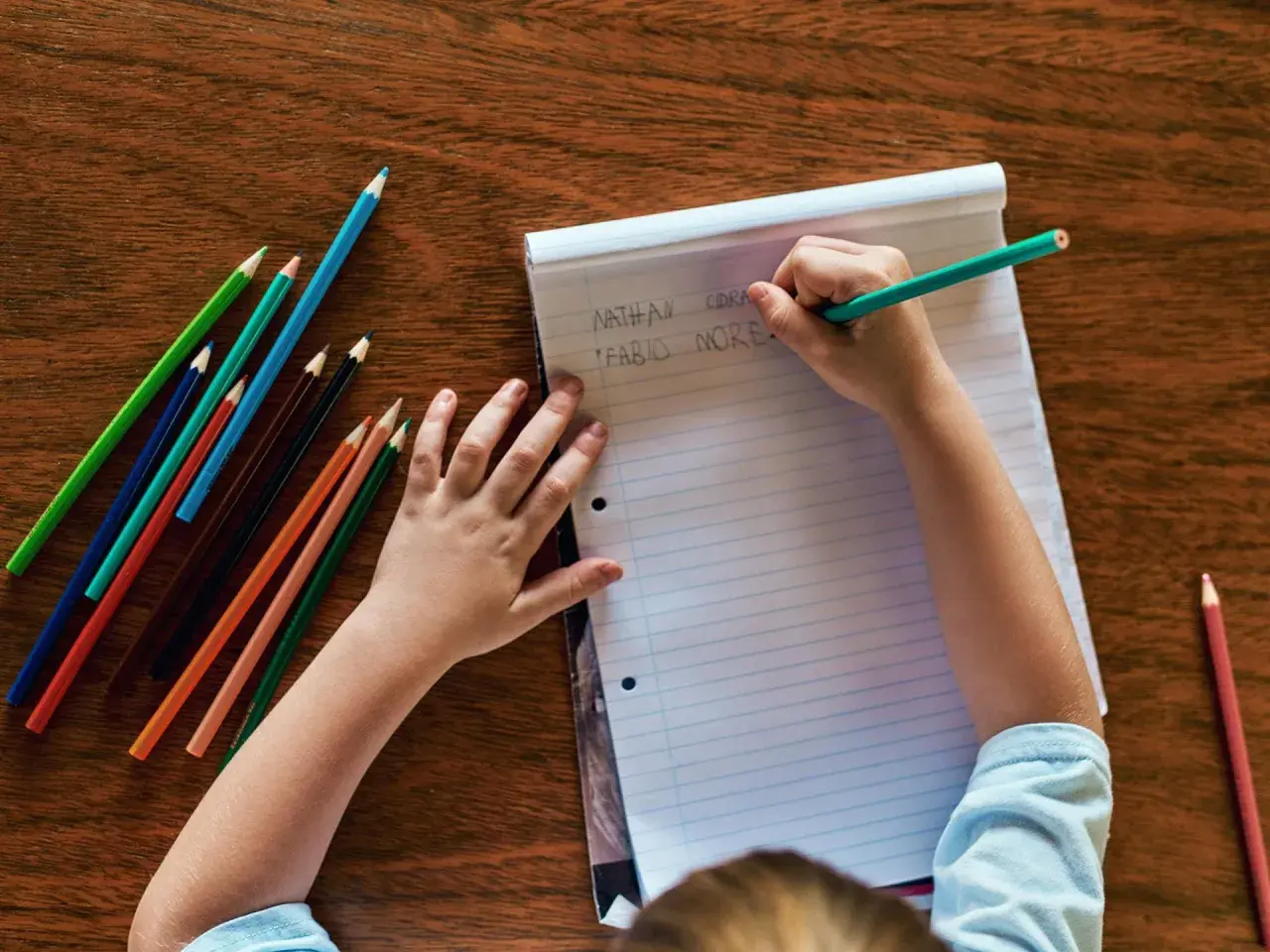 Kind schreibt Namen auf Papier, Teil der schuleingangsuntersuchung was wird gemacht. Buntstifte liegen bereit.