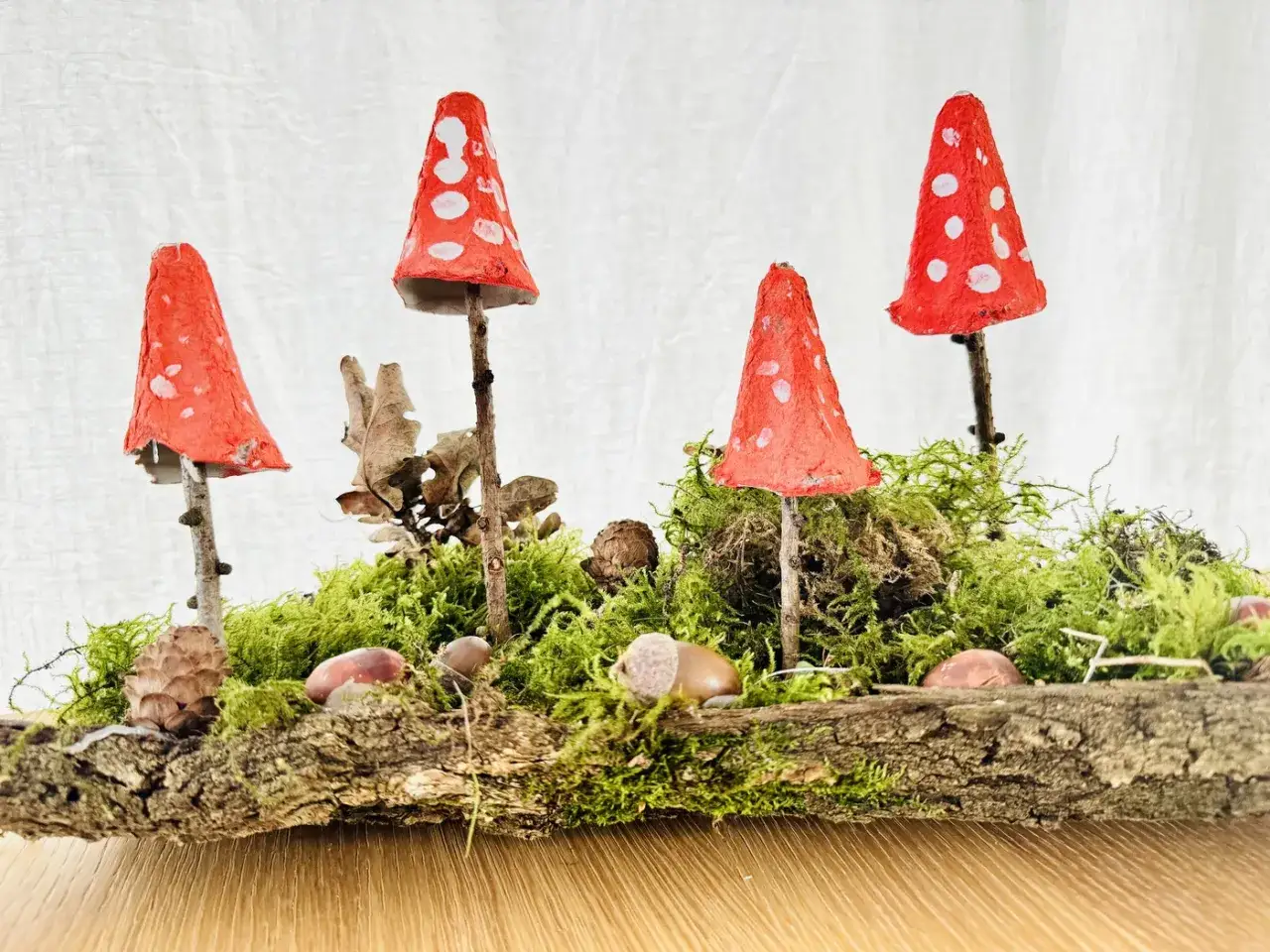 Vier rote Fliegenpilze, gebastelt mit Kindern, stehen auf Moos und Holz. Ein herbstliches Bastelprojekt.
