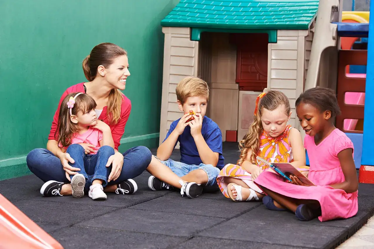 Ein fr&ouml;hlicher Morgenkreis im Kindergarten: Kinder und Erzieherin sitzen im Kreis, lesen und lachen.