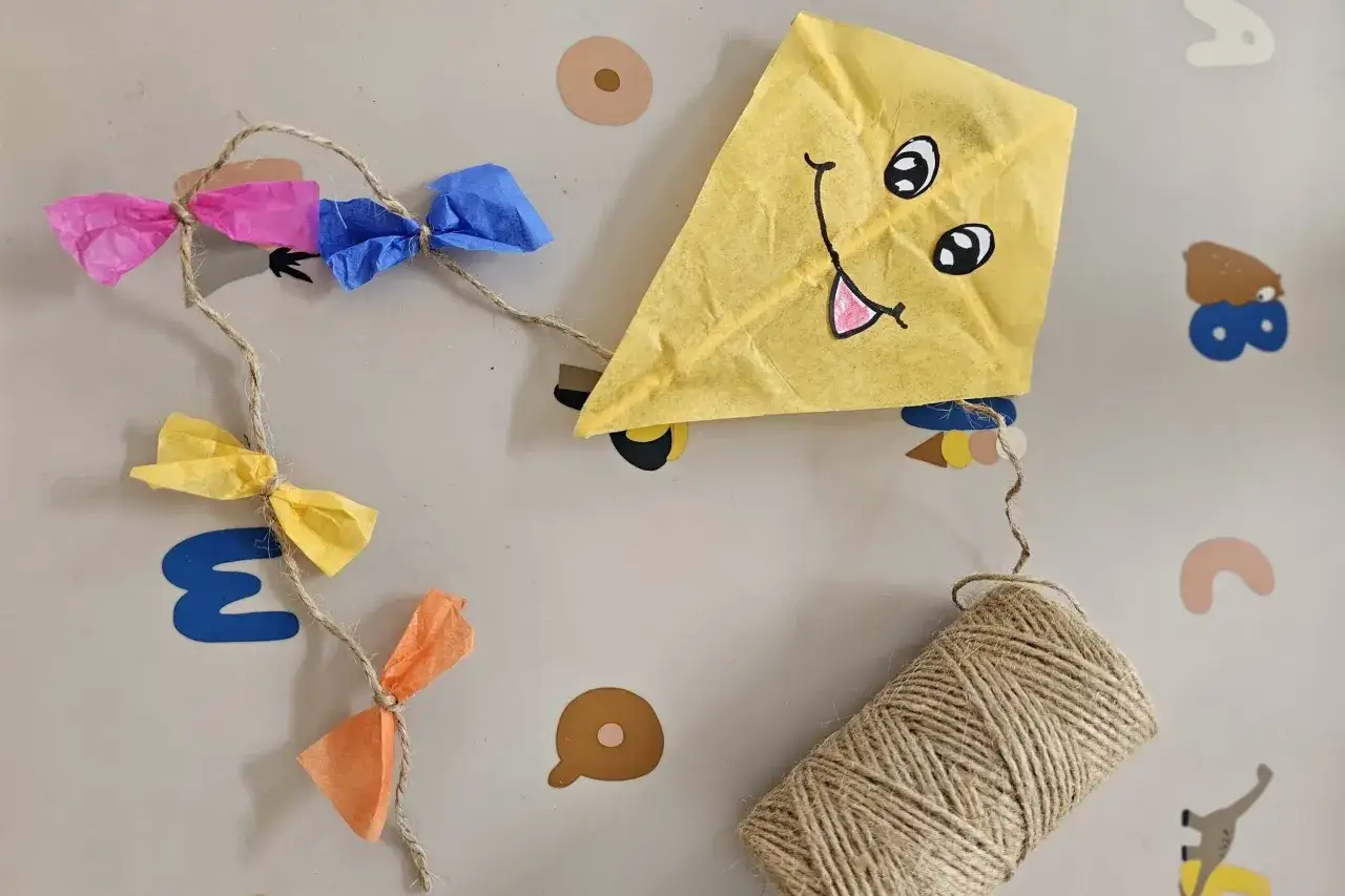Ein gelber Papierdrachen mit lustigem Gesicht und bunten Papierbanderolen h&auml;ngt an einer Schnur. Perfekt zum Drachen basteln!