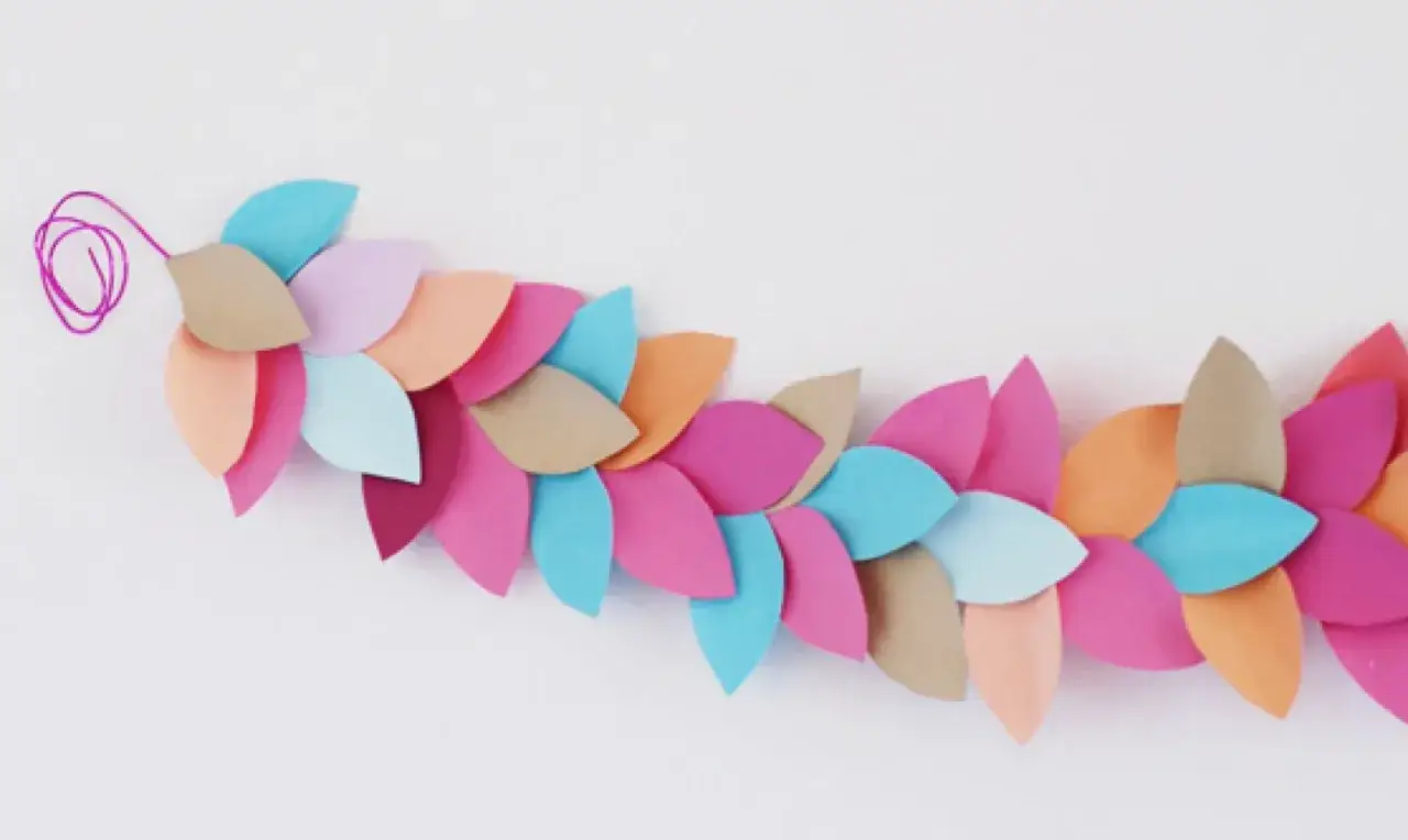 Bunte Bl&auml;tter aus Papier, die zu einer Girlande gebastelt wurden. Ein lila Faden h&auml;ngt am Anfang.
