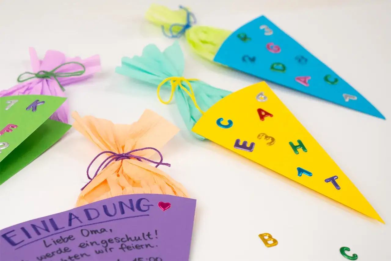 Bunte Zuckertüten mit Buchstaben und Zahlen, dazu eine Einladung zur Einschulung.