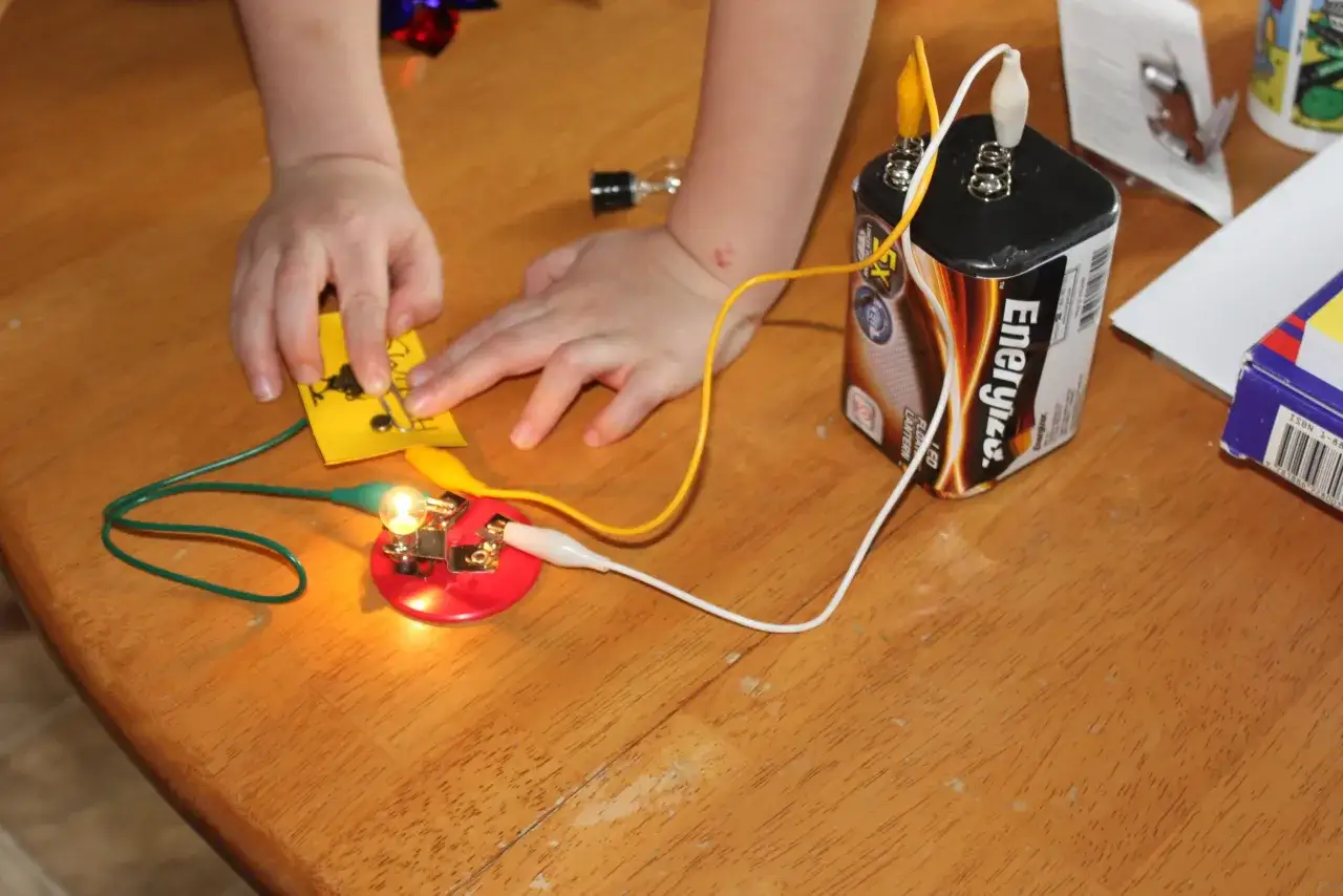 Kinder bauen einen Stromkreis. Eine Glühbirne leuchtet, während sie mit einer Batterie verbunden ist. Ein spannendes Experiment für die Grundschule.