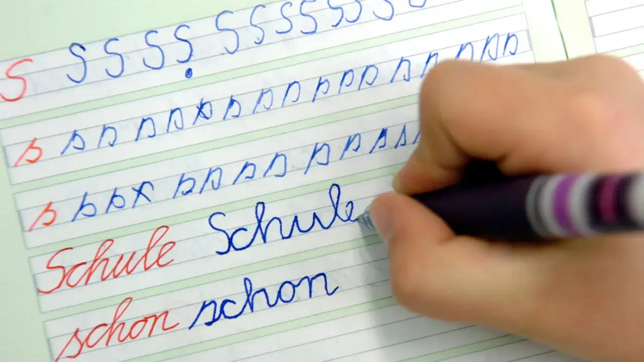 Kind &uuml;bt Schreibschrift. Auf dem linierten Blatt sind die druckschrift buchstaben S, b und W&ouml;rter wie 
