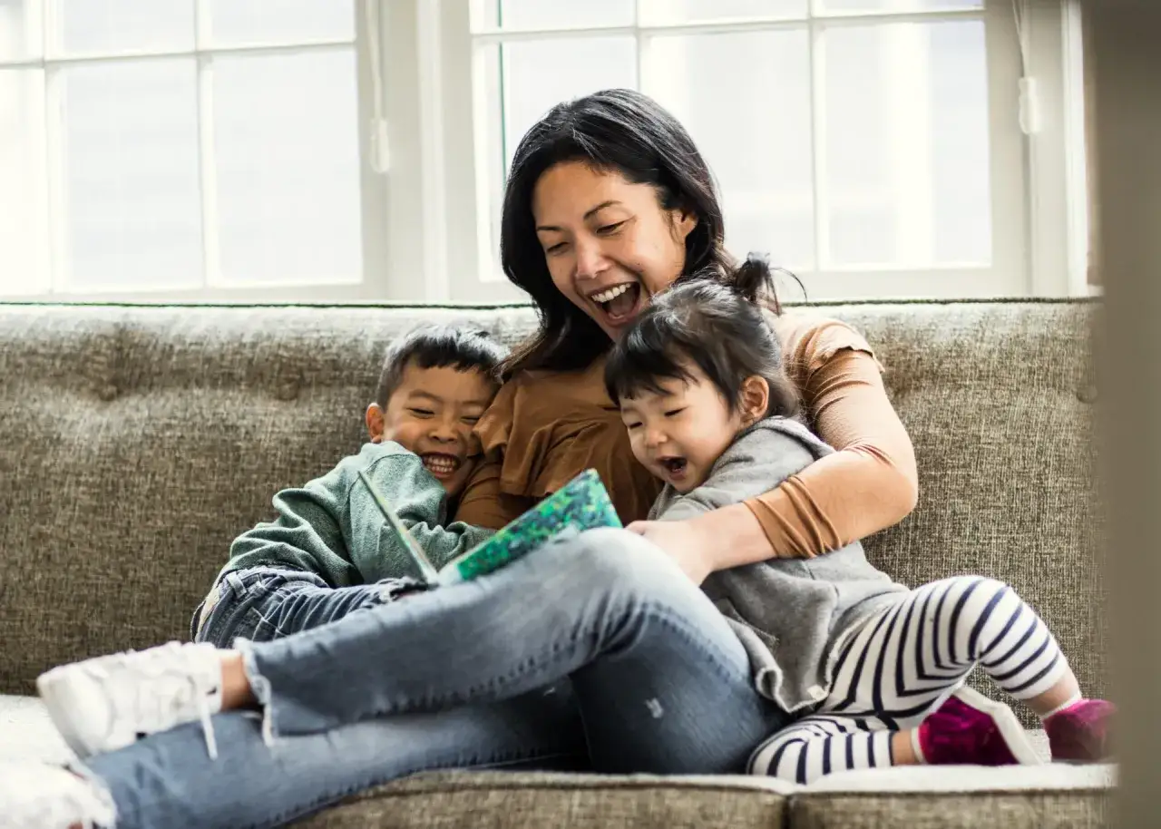 Mutter liest ihren Kindern ein Buch vor. Die Kinder lachen und sind begeistert. Ein sch&ouml;ner Moment, um lesen lernen kinder zu f&ouml;rdern.